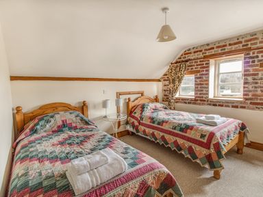 A bedroom with two single wooden beds and patchwork quilts near two windows with floral curtains at Manor Farm Barn in Dewlish