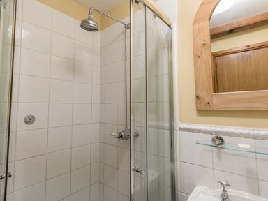 A tiled shower with a glass door and mirror above a sink in a bathroom at Manor Farm Barn in Dewlish