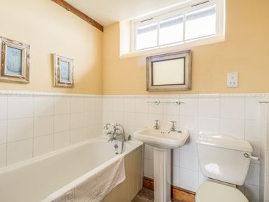 A bathroom with a bathtub sink toilet and three framed pictures on the walls at Manor Farm Barn in Dewlish