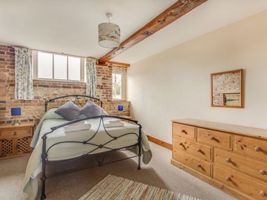 A bedroom with a metal bed frame two pillows two bedside cabinets with lamps a wooden dresser a mirror and windows at Manor Farm Barn in Dewlish