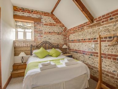 A bedroom with exposed brick walls a bed with green pillows and towels and wooden coat rack at Manor Farm Barn in Dewlish