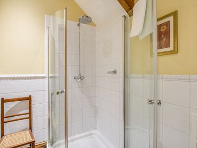 A bathroom with a glass shower enclosure a wooden chair and a framed flower picture on the wall at Manor Farm Barn in Dewlish