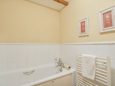 A bathroom with a bathtub towel rack and two framed floral pictures on the wall at Manor Farm Barn in Dewlish