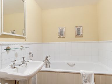 A bathroom with a pedestal sink and a bathtub with white tiles on the walls at Manor Farm Barn in Dewlish