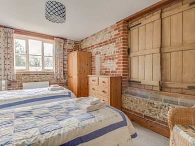 A bedroom with two single beds a wooden dresser and wardrobe exposed brick walls and a window with curtains at Manor Farm Barn in Dewlish