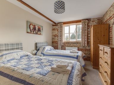 A bedroom with two single beds a wooden wardrobe and chest of drawers and a window with curtains at Manor Farm Barn in Dewlish
