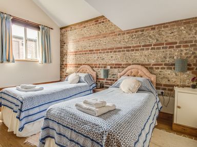 A bedroom with two single beds and brick feature wall at Manor Farm Barn in Dewlish