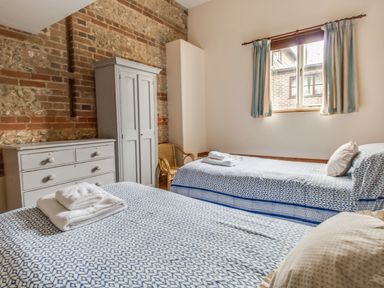A bedroom with two single beds a white wardrobe a white dresser and a window with curtains at Manor Farm Barn in Dewlish