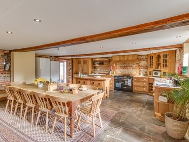 A kitchen and dining area with a long wooden table and chairs a kitchen island and wooden cabinets at Manor Farm Barn Dewlish