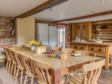 A kitchen with a wooden dining table and chairs with bread fruit and flowers at Manor Farm Barn in Dewlish
