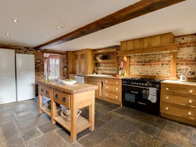 A kitchen with wooden cabinets an island in the center and two white refrigerators against a brick wall at Manor Farm Barn in Dewlish