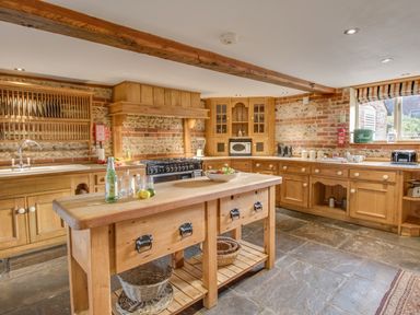 A kitchen with wooden cabinets an island and a stone floor at Manor Farm Barn in Dewlish
