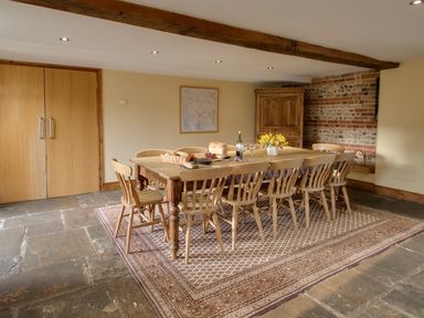 A dining room with a wooden table and chairs on a patterned rug at Manor Farm Barn in Dewlish