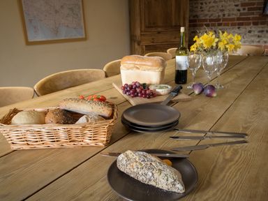 A dining table with bread, grapes, wine, glasses, knives, figs and flowers at Manor Farm Barn in Dewlish