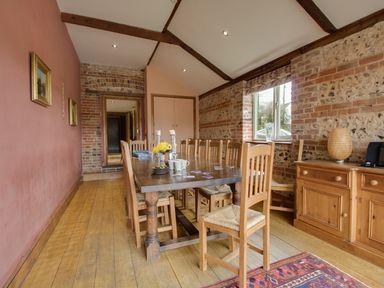 A dining room with a long wooden table and chairs near a window with brick walls at Manor Farm Barn in Dewlish