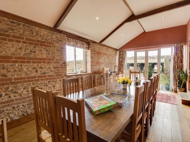 A dining room with a long wooden table and chairs next to stone walls and large windows at Manor Farm Barn in Dewlish