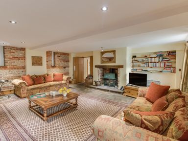A living room with two patterned sofas a wooden coffee table a fireplace and bookshelves at Manor Farm Barn in Dewlish