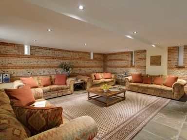 A sitting room with patterned sofas and red cushions around a wooden coffee table on a large rug at Manor Farm Barn in Dewlish