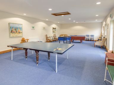 A game room with a table tennis, foosball, and pool table with chairs and paintings on the walls at Manor Farm Barn in Dewlish