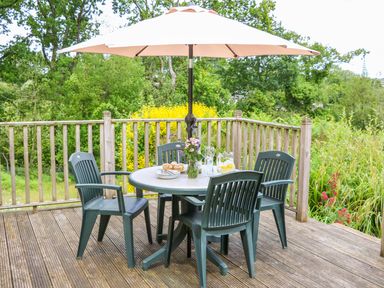A wooden deck with a round table and four plastic chairs under a large umbrella at Woodstock Cottage in Birchill near Chardstock