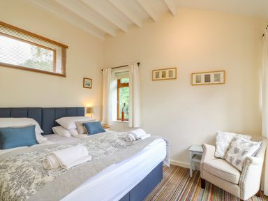 A bedroom with a double bed pillows and towels an armchair with cushions and framed pictures on the wall at Woodstock Cottage in Birchill near Chardstock