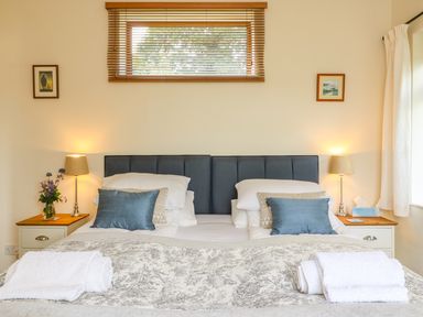 A bedroom with two beds joined together two bedside tables with lamps flowers and tissues at Woodstock Cottage Birchill near Chardstock