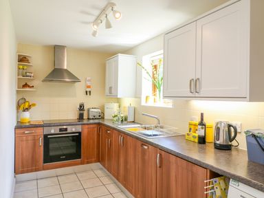 A kitchen with wooden lower cabinets white upper cabinets tiled floor and various kitchen appliances at Woodstock Cottage in Birchill near Chardstock