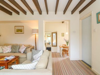 A living room with beige sofas, a wooden coffee table, a floor lamp, and a dining area with a wooden table and chairs at Woodstock Cottage in Birchill near Chardstock