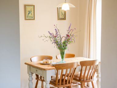 A dining area with a wooden table and chairs a vase with flowers and muffins on the table at Woodstock Cottage Birchill near Chardstock