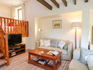 A living room with sofas a wooden coffee table a television and wooden staircase at Woodstock Cottage in Birchill near Chardstock