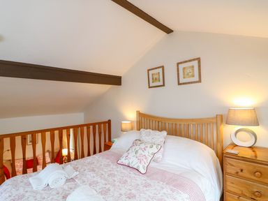 A bedroom with a double bed two bedside tables with lamps and two framed pictures on the wall at Woodstock Cottage in Birchill near Chardstock