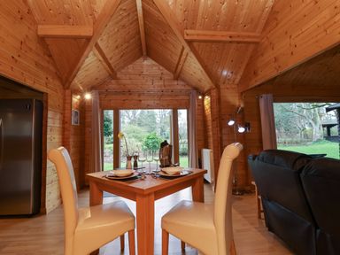 A wooden dining room with a table set for two and cream chairs at Woodpeckers in Willand