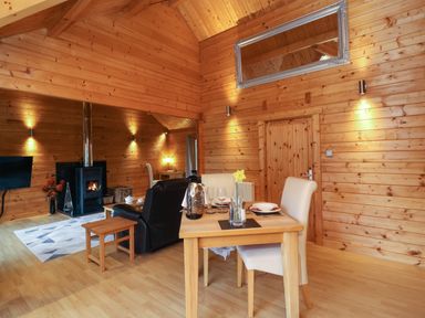 A wooden interior with a dining table and chairs a wood stove and a sitting area at Woodpeckers in Willand