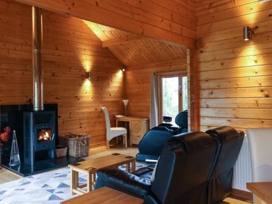 A living room with a wood burning stove a wicker basket a wooden coffee table black leather chairs a white chair and a desk at Woodpeckers in Willand