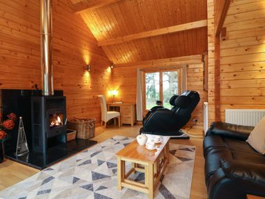 A wooden living room with a fireplace a black massage chair a black sofa and a wooden coffee table with tea set at Woodpeckers in Willand