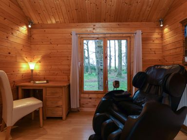 A wooden room with a desk chair lamp and massage chair next to a window with curtains at Woodpeckers in Willand