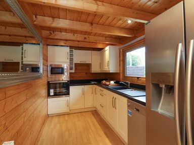 A kitchen with wooden walls and ceiling white cabinets black countertop stainless steel refrigerator microwave oven and dishwasher at Woodpeckers in Willand