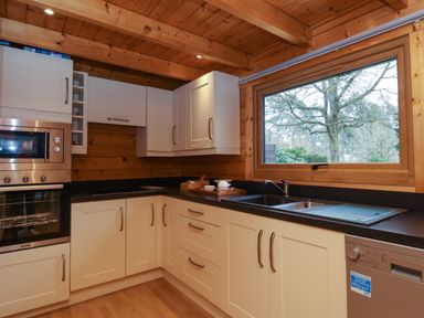 A kitchen with cream cabinets a black countertop a double sink dishwasher built in oven and microwave and a window showing trees at Woodpeckers in Willand