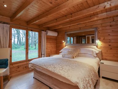 A bedroom with a bed pillows and a large mirror on the wooden wall at Woodpeckers in Willand