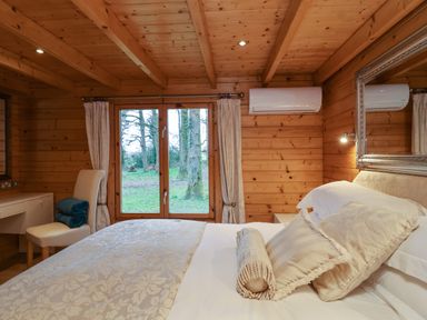 A bedroom with wooden walls and ceiling a bed with pillows a chair with folded blankets a desk and a window showing trees at Woodpeckers in Willand