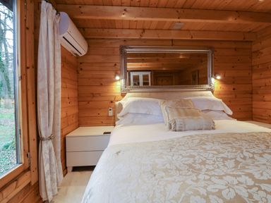A bedroom with a large bed white bedside table air conditioner and a large mirror on wooden walls at Woodpeckers in Willand