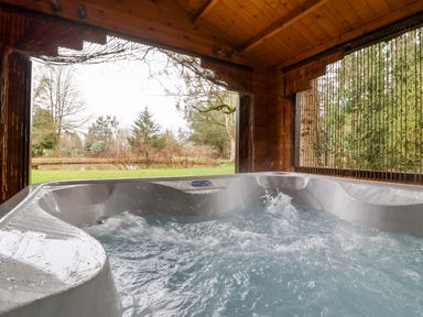 A bubbling hot tub inside a wooden gazebo overlooking a garden with trees at Woodpeckers in Willand