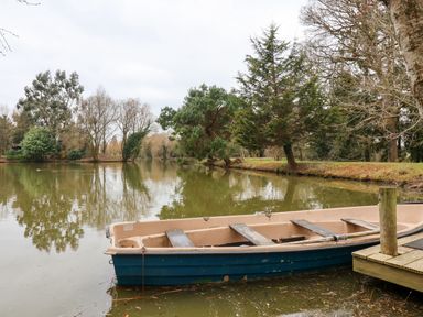 A small boat tied to a wooden dock on a lake surrounded by trees at Woodpeckers in Willand