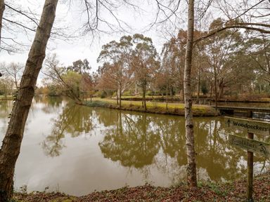 A river surrounded by trees with a wooden sign pointing to Woodpeckers and Kingfishers at Woodpeckers in Willand