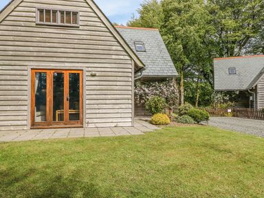 An exterior view of wooden cladded buildings with patios a garden and trees at Trevinny Lodge No 37 in Davidstow near Boscastle