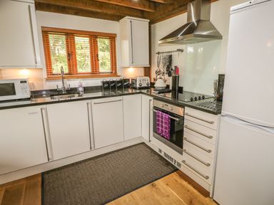 A kitchen with white cabinets black countertops a stove a microwave a refrigerator and a window with wooden blinds at Trevinny Lodge No 37 Davidstow near Boscastle