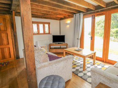 A living room with wooden beams a television and glass doors at Trevinny Lodge No 37 Davidstow near Boscastle