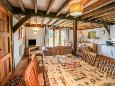 A dining area with a table and chairs next to a living room with sofas a TV and wooden beams at Trevinny Lodge No 37 in Davidstow near Boscastle