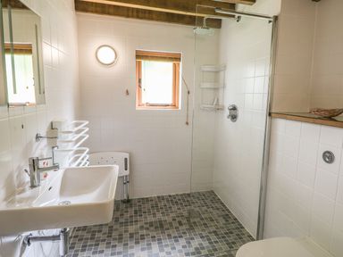 A bathroom with a sink a walk-in shower with a glass panel a small window and a white chair at Trevinny Lodge No 37 Davidstow near Boscastle