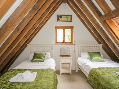 A bedroom with two single beds green pillows and bed covers a nightstand with two woven lamps under a small window at Trevinny Lodge No 37 Davidstow near Boscastle